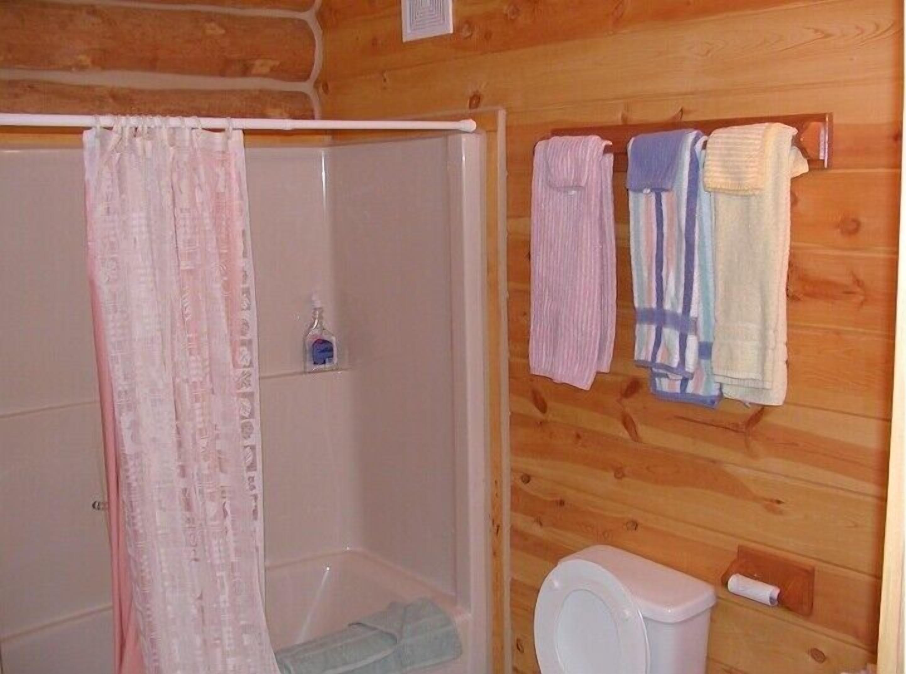 Un baño de cabaña de madera con ducha, inodoro y toallas colgadas en la pared.