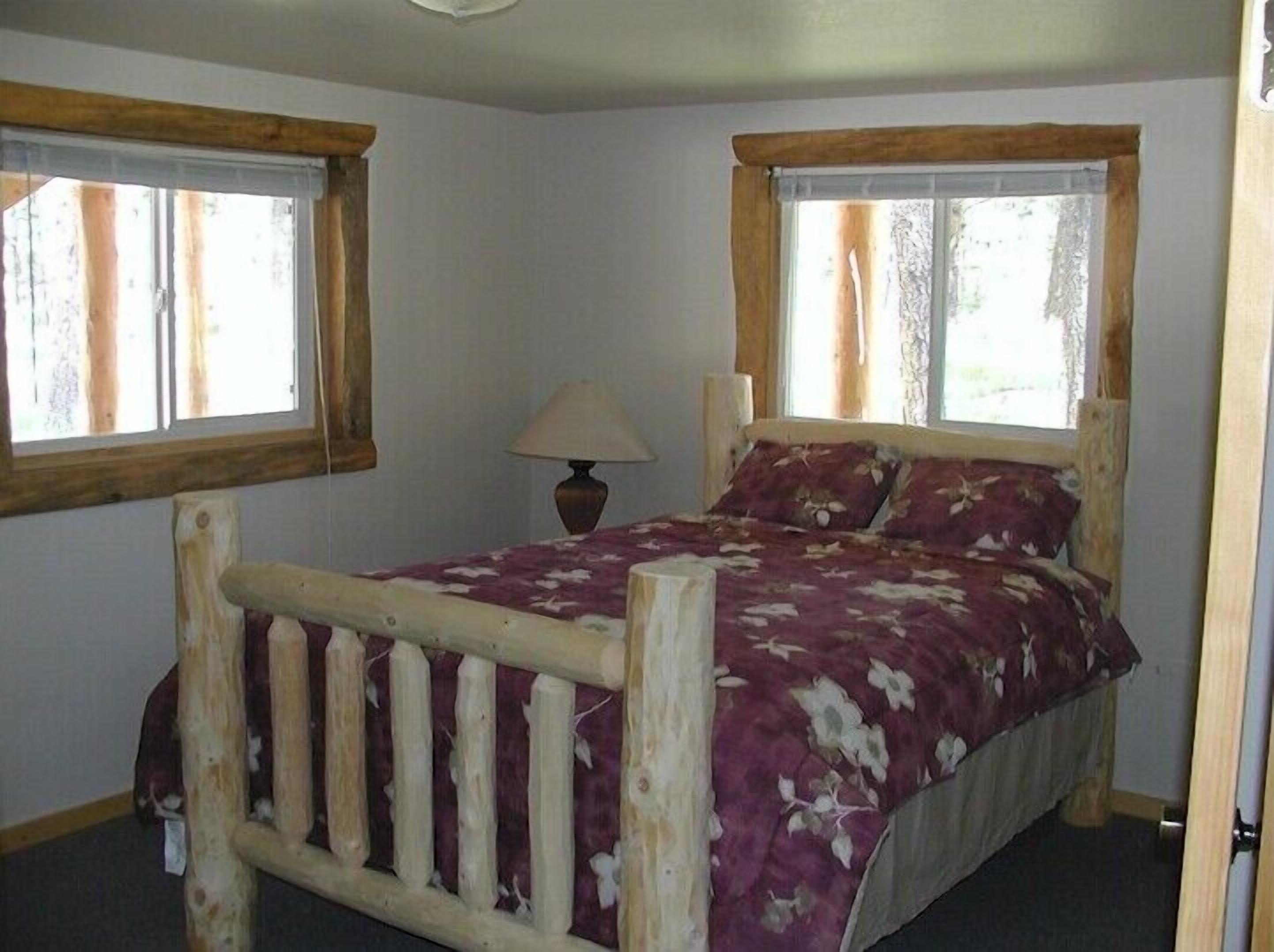 A single bed with a wooden frame and floral bedding in a room with two windows and a lamp.