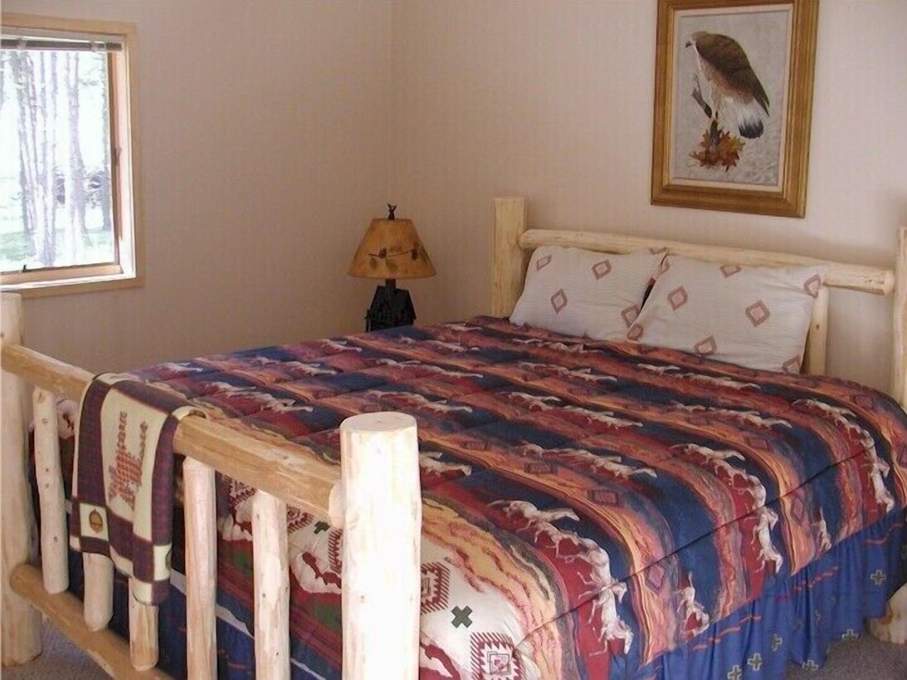 Een slaapkamer met een houten bedframe, een bedovertrek met dessin, een nachtkastje met lamp en een fotolijst aan de muur.