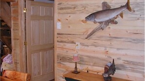 A room with a wooden door, a wooden wall with a fish mural, a small table with a lamp, and a chair. - Papoose (Custer)