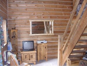 A log cabin room with a wooden TV stand, a small cabinet, and a window with a decorative mirror. - Papoose (Custer)