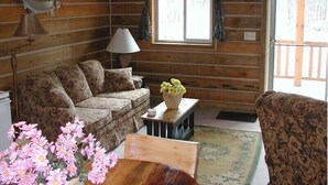 A cozy cabin interior with a floral-patterned sofa, a small table with a vase of flowers, and a lamp. - Papoose (Custer)