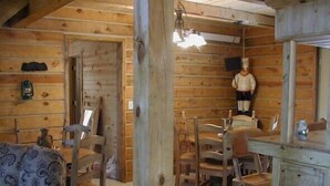 A rustic cabin interior with wooden walls, a dining table, chairs, a sofa, and a dresser. - Desperado (Custer)