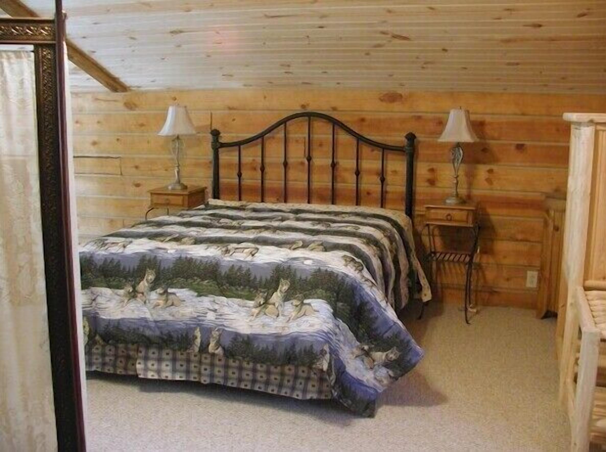 A wooden cabin bedroom with a bed, two bedside lamps, and a wooden headboard.