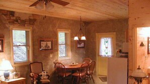 A cozy dining area with a wooden table and chairs, a ceiling fan, and a kitchen visible through an open door.