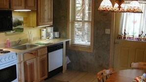 A kitchen with wooden cabinets, a stove, a dishwasher, a window with blinds, and a dining table with chairs.