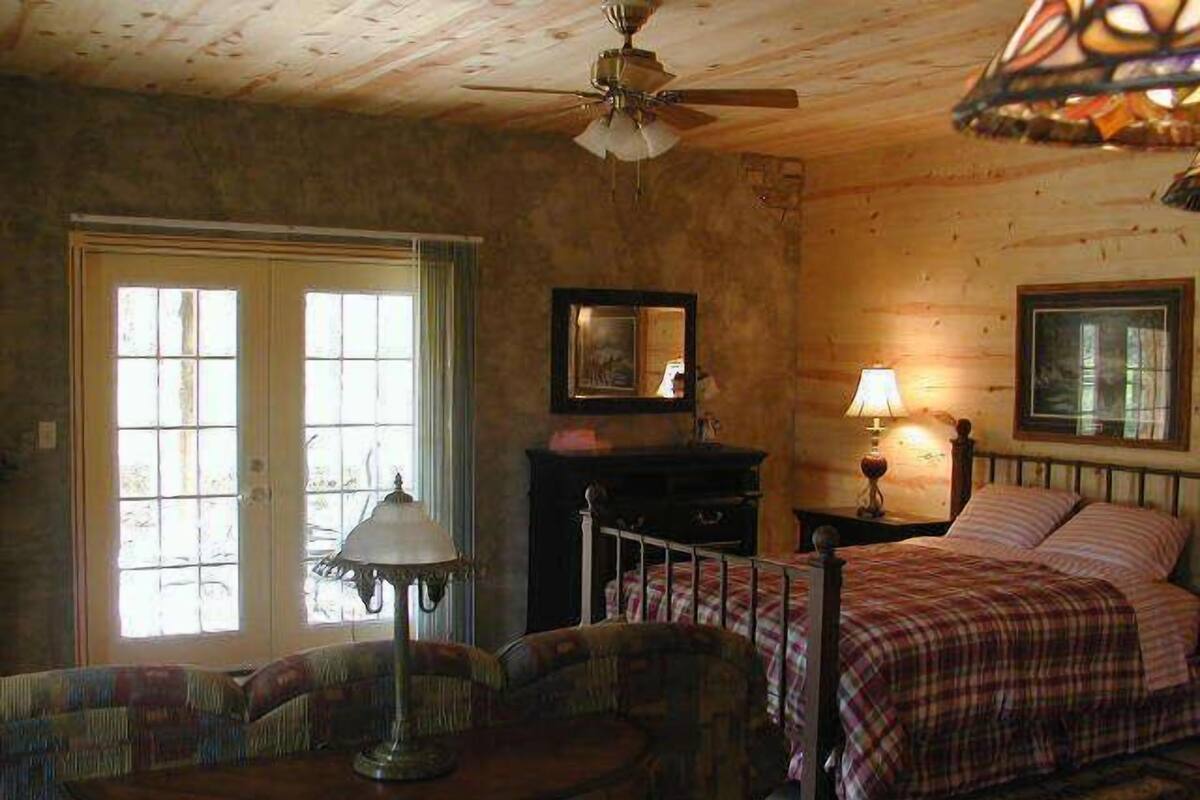 A cozy room with a bed, a desk, a chair, a lamp, and a ceiling fan.
