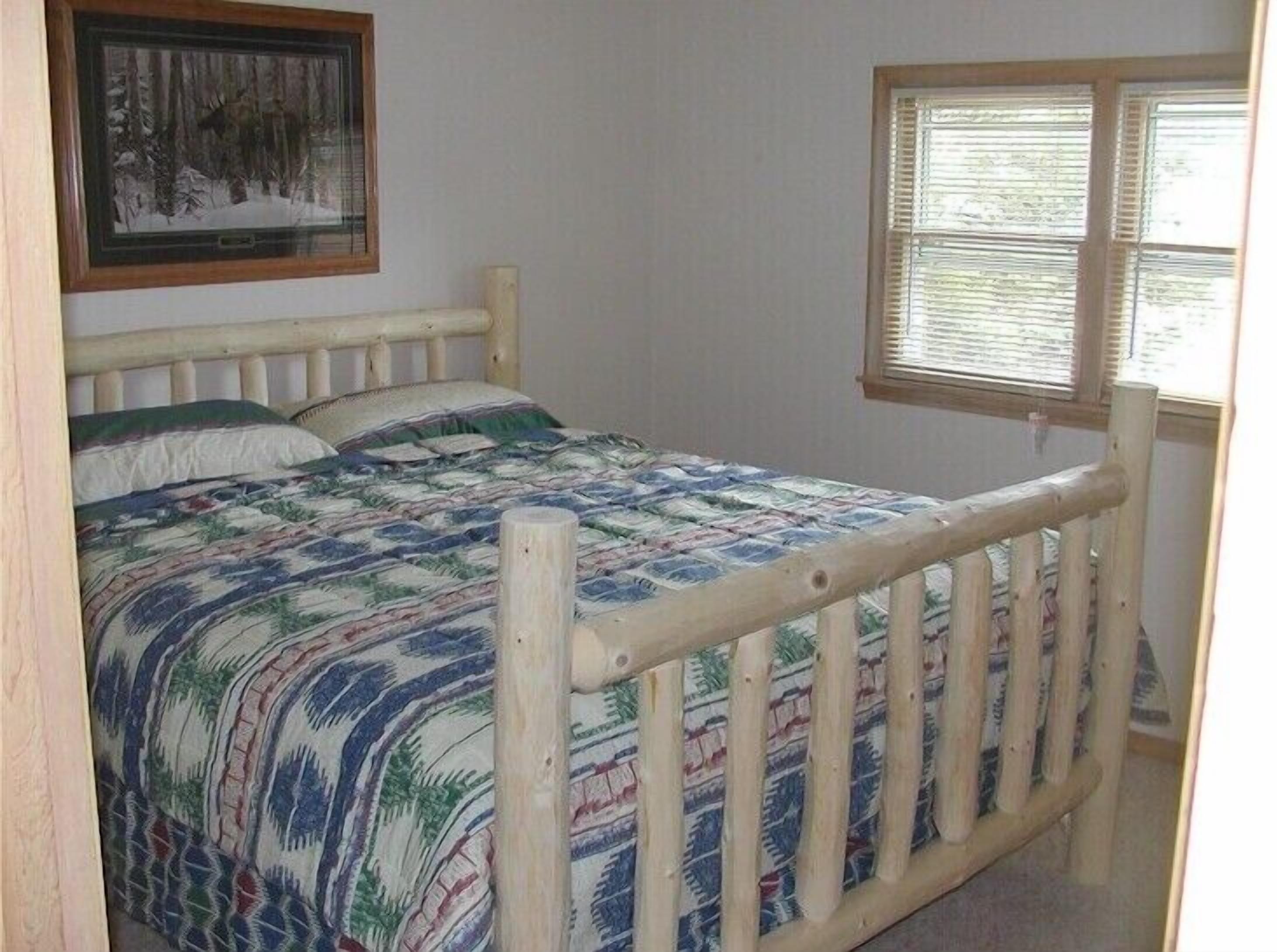 Un dormitorio con cabecera de cama de madera, colcha, un cuadro en la pared y una ventana con persianas.