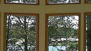 A room with four windows, each with a view of a tree and a grassy area. - Thunderheart (Custer)