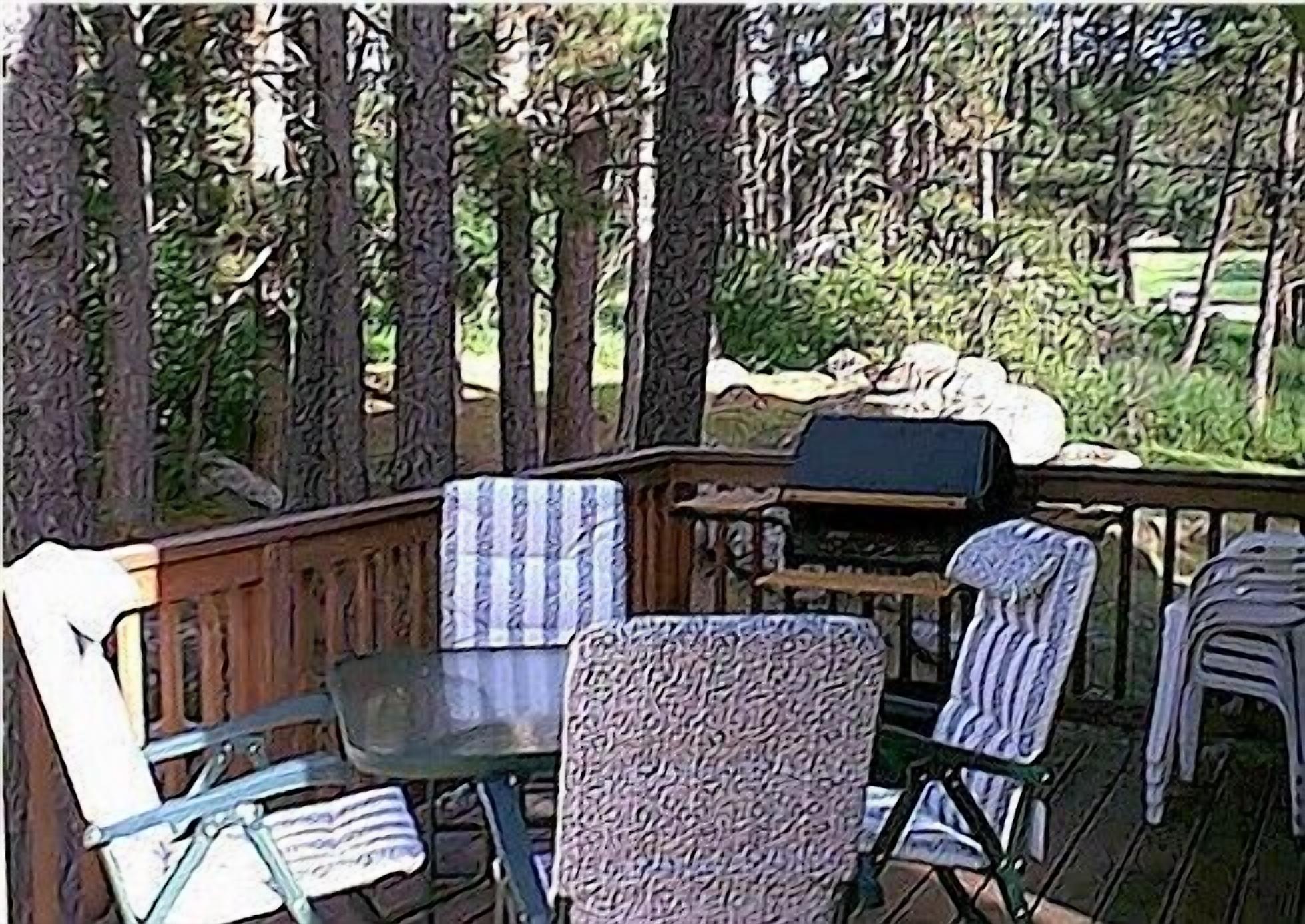 Eine Holzterrasse mit Grill, zwei Stühlen und einem Tisch.