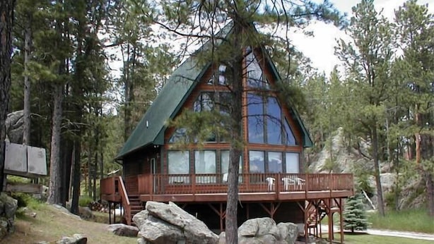 A cabin with a large glass window, wooden deck, and a stone foundation. - Thunderheart (Custer)
