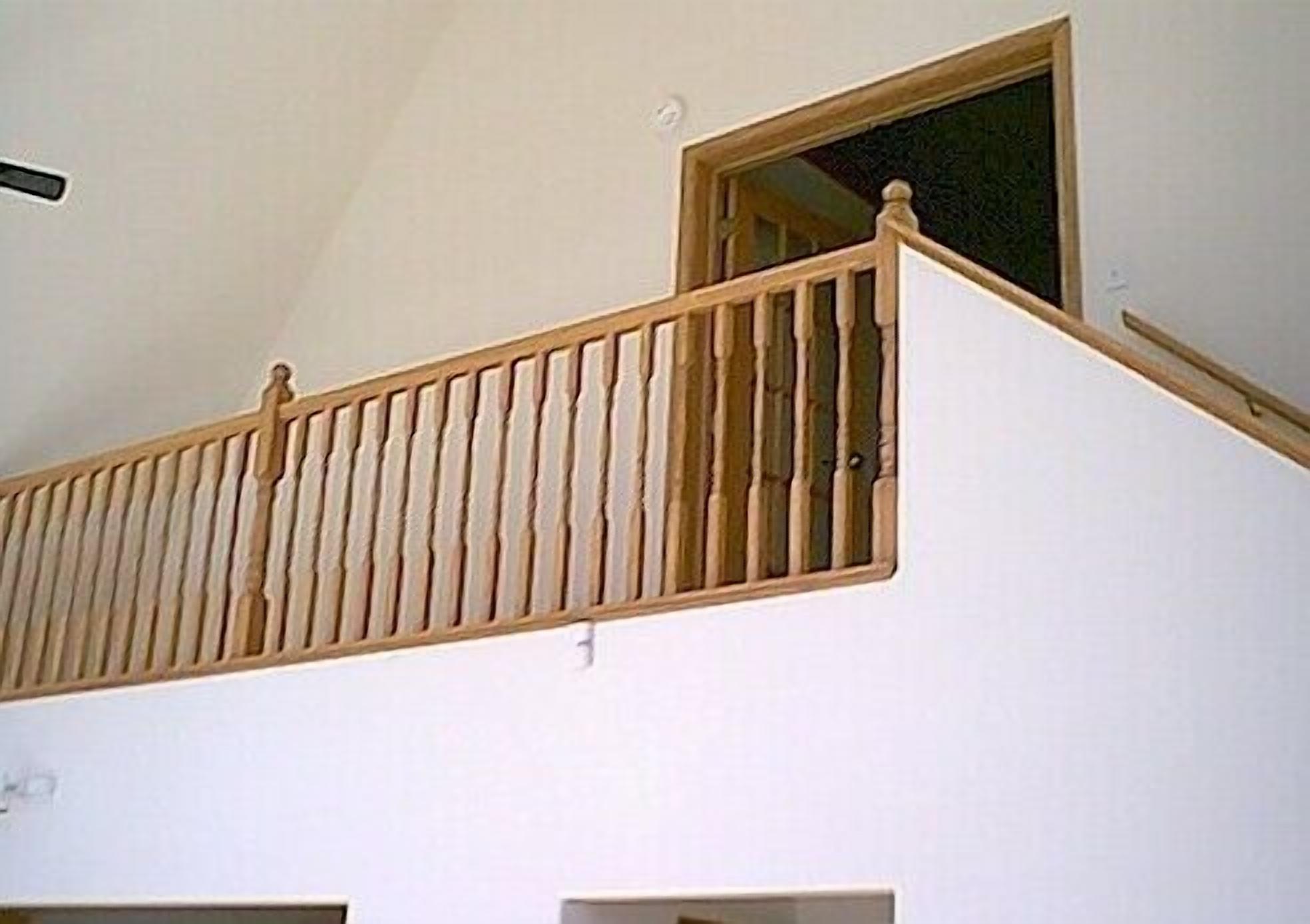 A white interior with a wooden balcony railing and a window.