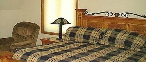 Ein Schlafzimmer mit einem hölzernen Kopfende, einer karierten Tagesdecke, einem Nachttisch mit Lampe und einem Sessel.