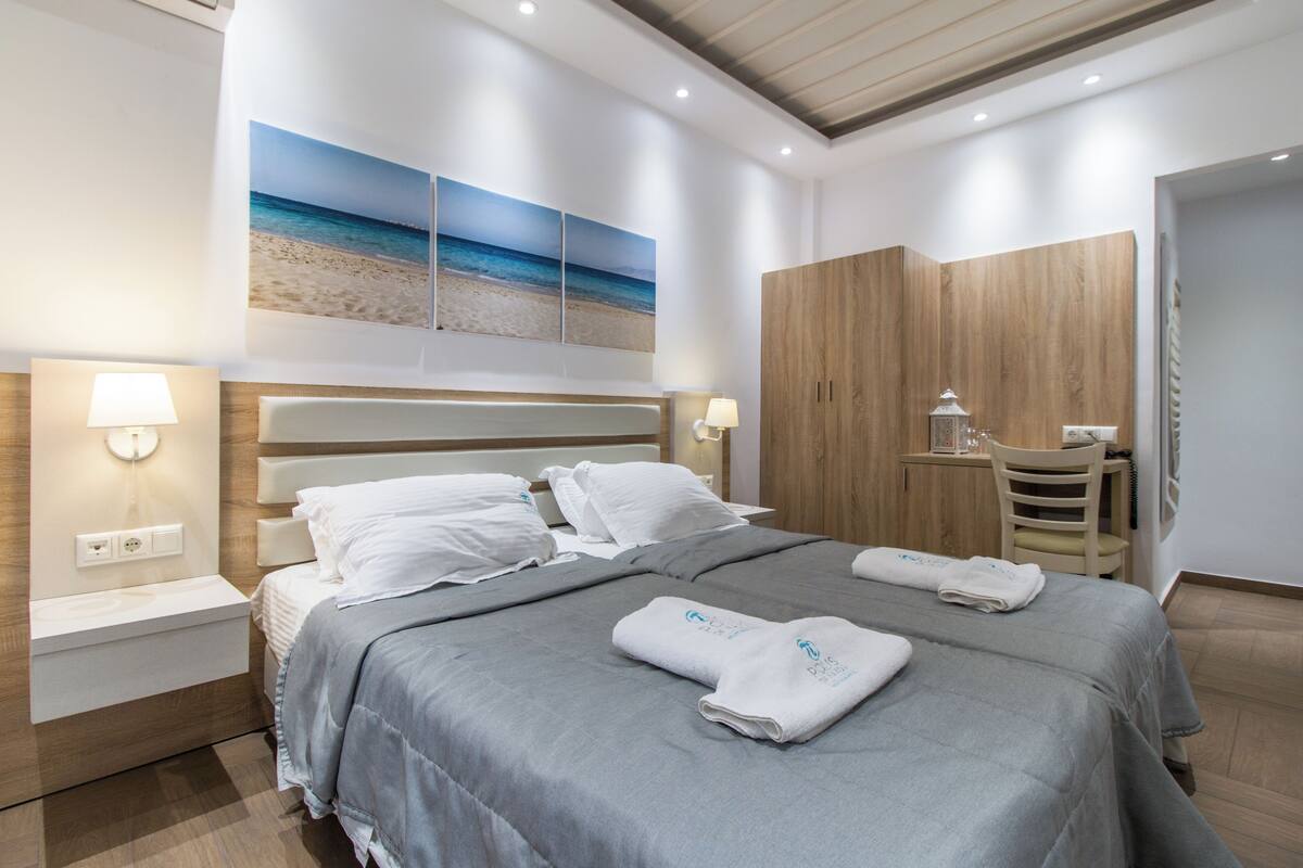 Een moderne hotelkamer met een groot bed, twee nachtkastjes, een houten garderobe en een bureau met een stoel.