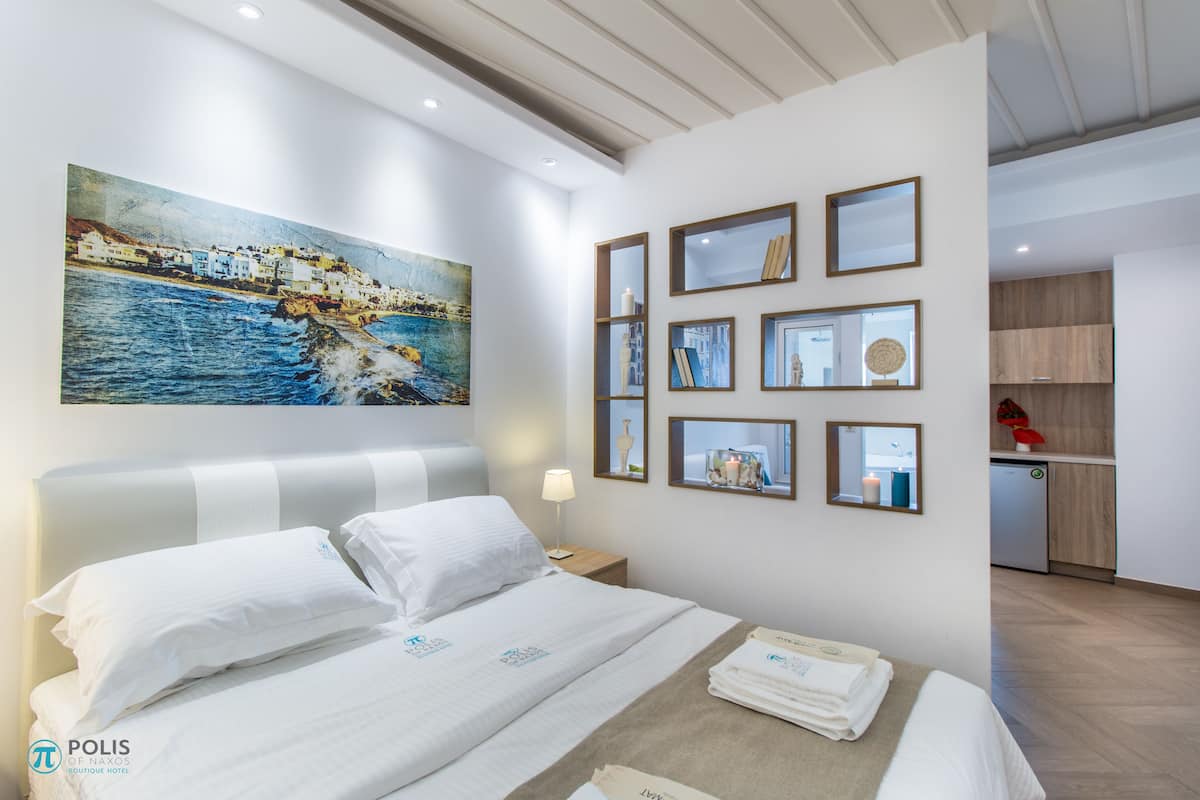 Een hotelkamer met een groot bed, een schilderij van een kustlandschap en enkele ingelijste foto's aan de muur.
