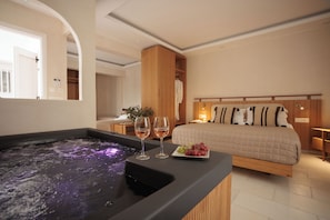 A bedroom with a bed, a hot tub, and two glasses of wine on a tray.