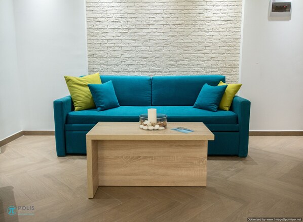 A teal sofa with yellow and green cushions, a wooden coffee table with decorative items, and a white brick wall.