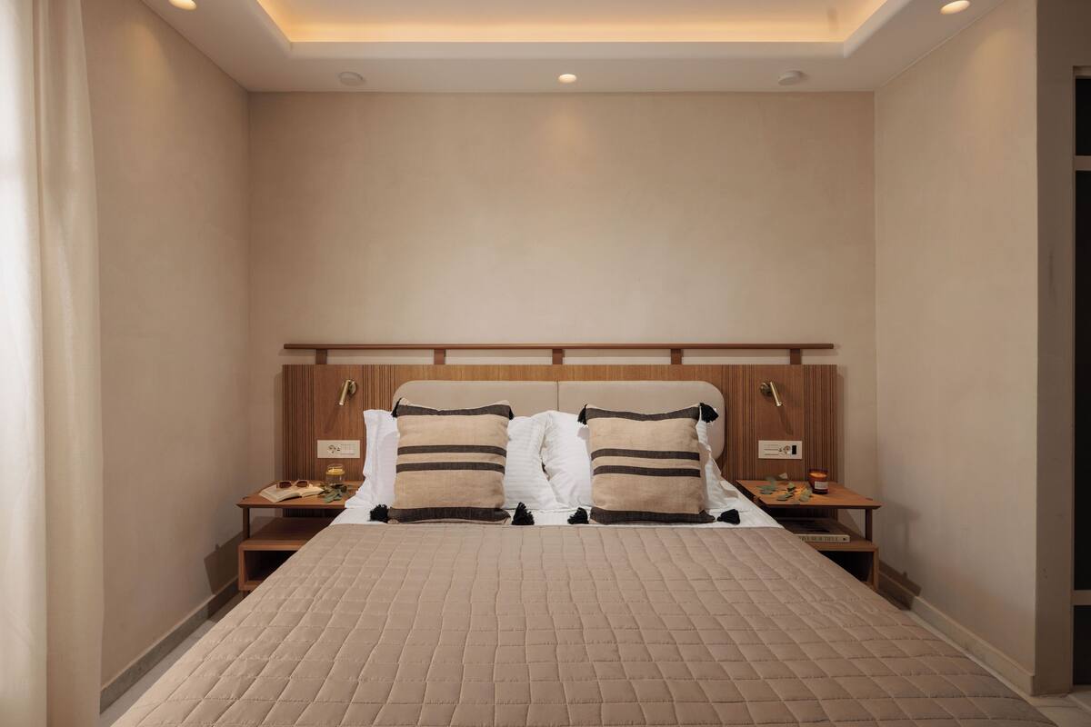 Een slaapkamer met een groot bed, houten hoofdbord, nachtkastjes en een nachttafeltje met een lamp.
