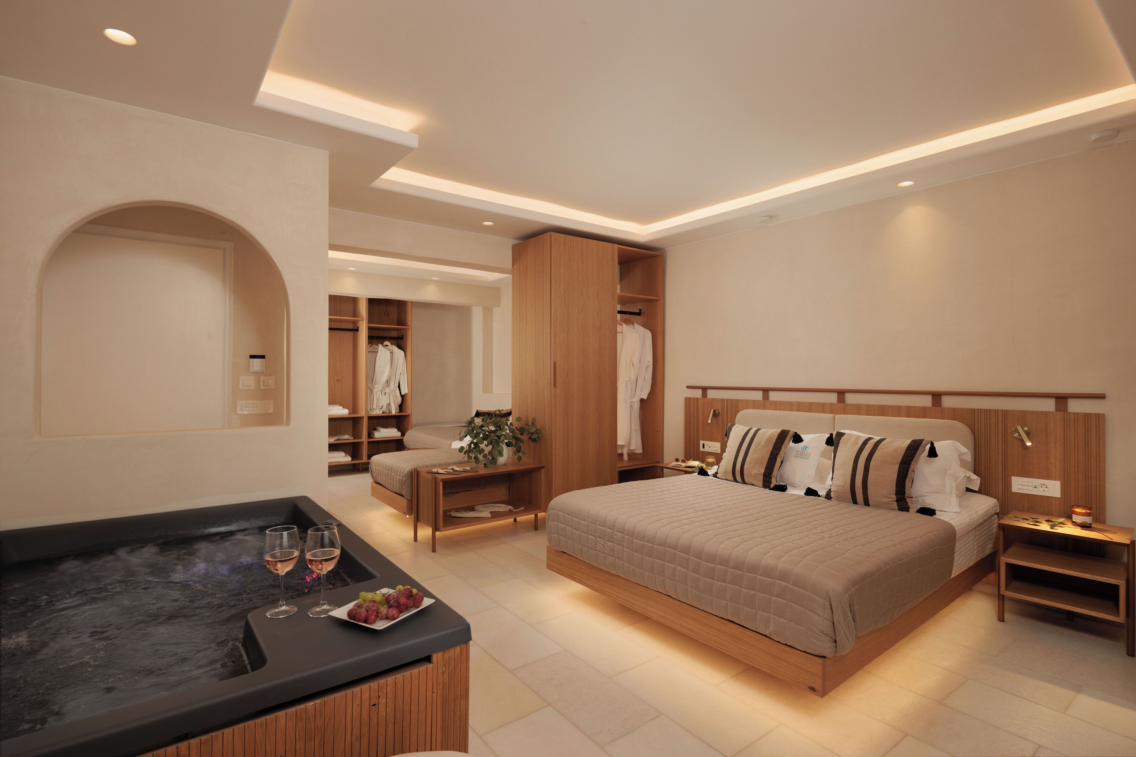 A modern bedroom with a large bed, a built-in wooden wardrobe, a small seating area, and a hot tub.