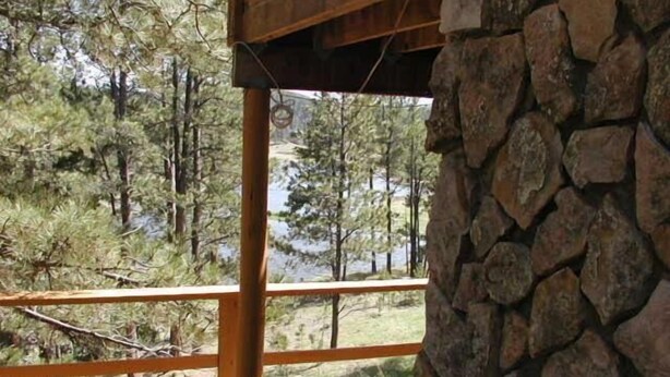 A wooden deck with a stone wall, overlooking a forested area and a body of water.