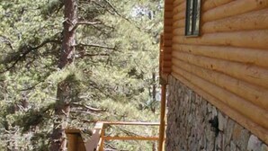 A wooden cabin with a stone foundation, a wooden deck, and a stone wall.