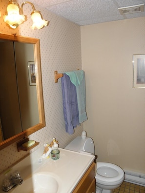 Un baño con un lavamanos blanco, un inodoro y un espejo con marco de madera. Hay dos toallas colgadas en un perchero.