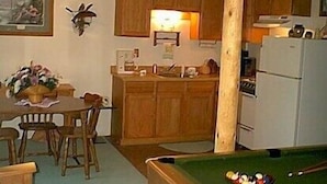 A compact kitchen with wooden cabinets, a dining area with chairs, and a pool table.