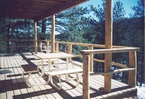 Una terraza de madera con mesas y sillas de picnic, rodeada de árboles.