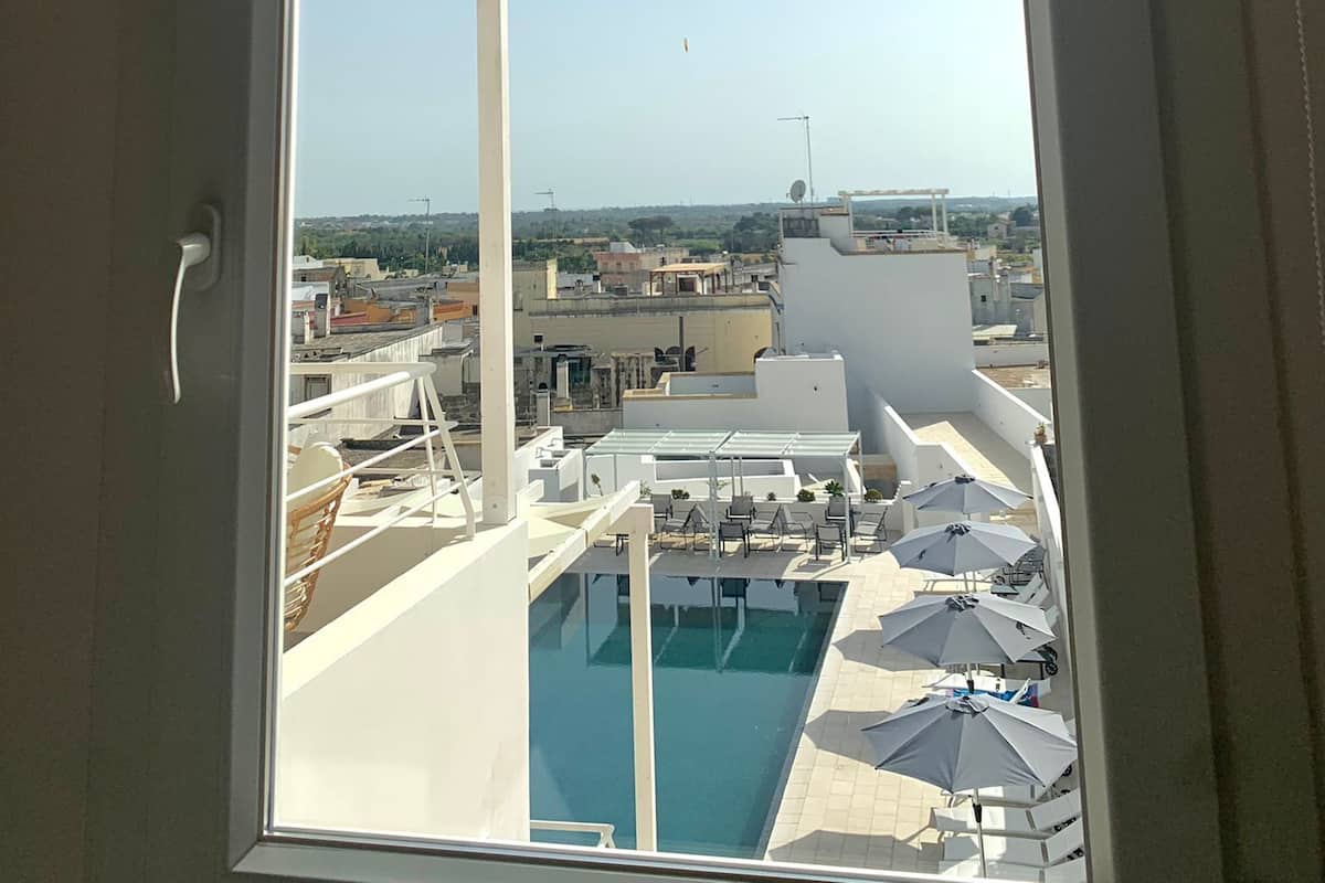 A view from a window overlooking a rooftop pool area with umbrellas and lounge chairs, and a clear sky.