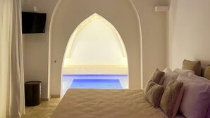 A bedroom with a large bed, a TV mounted on the wall, and a view through an arched window. - TS Residence (Sannicola)