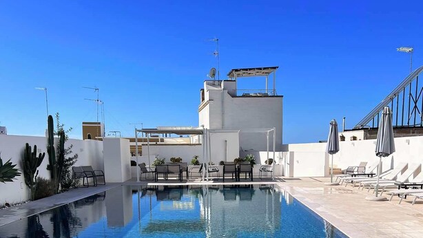 A clear swimming pool with lounge chairs and umbrellas, surrounded by white walls and cacti. - TS Residence (Sannicola)