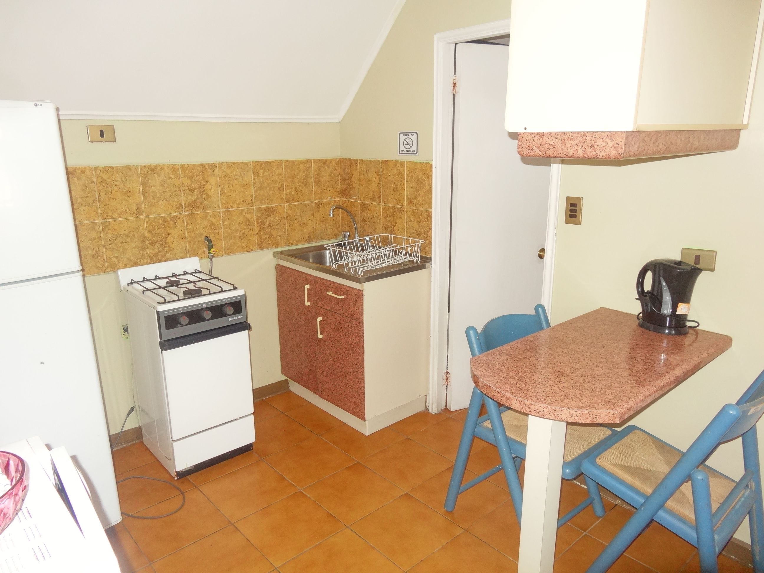 Une cuisine compacte équipée d’une cuisinière à gaz, d’un évier et d’une petite table à manger avec des chaises bleues.