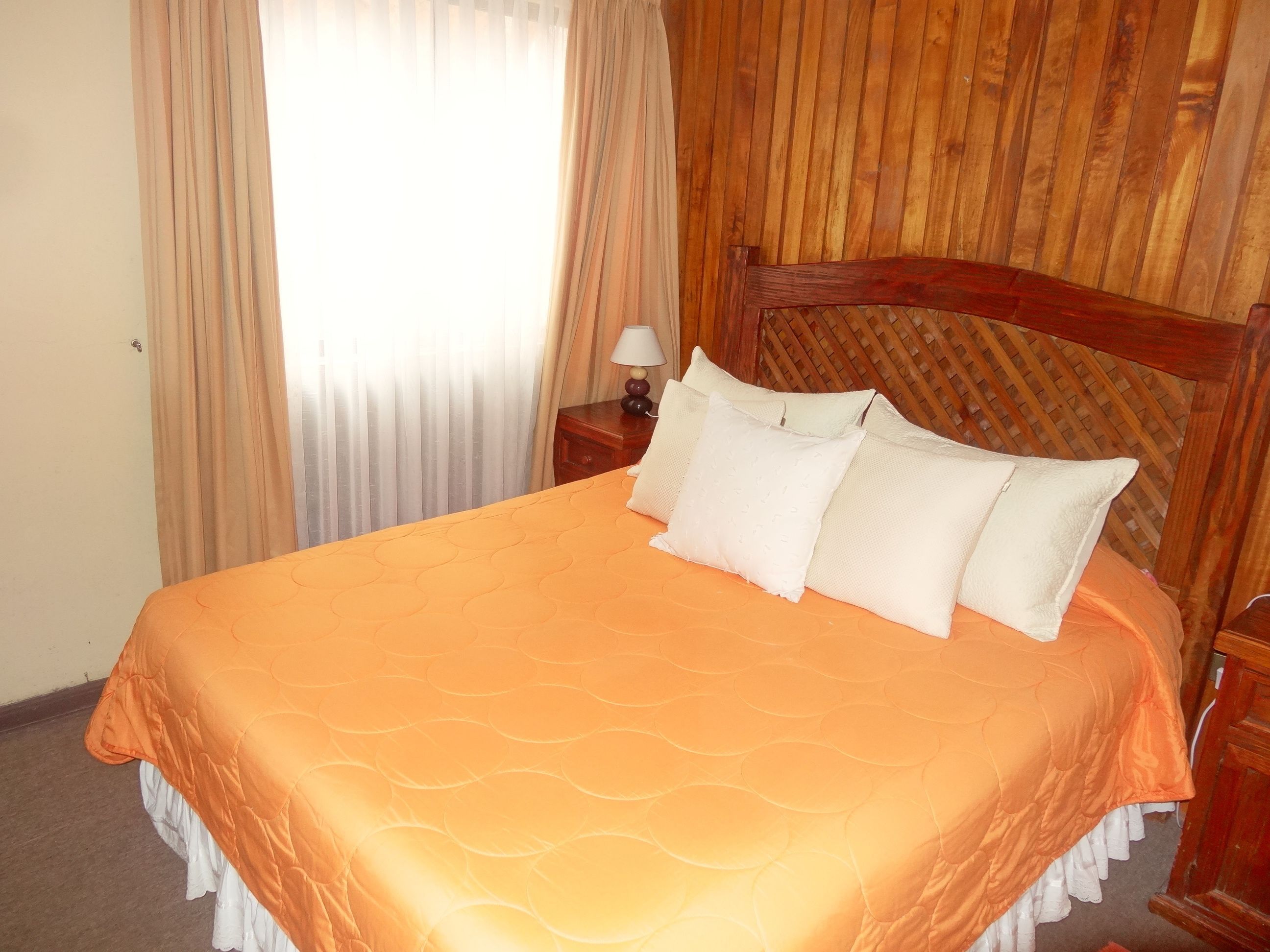 A bed with an orange quilt, wooden headboard, and white pillows.