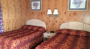 Una habitación con dos camas individuales, paredes de paneles de madera y dos lámparas fijadas a la pared.