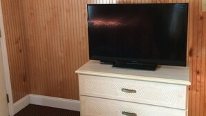 Ein Zimmer mit einer holzverkleideten Wand, einem Flachbildfernseher auf einer weißen Kommode und einem braunen Teppichboden.