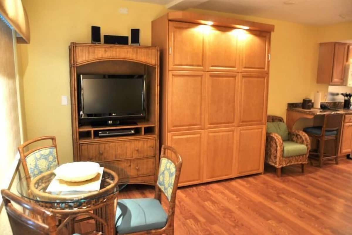 A living room with a television, wooden cabinets, wicker chairs, and a dining table.
