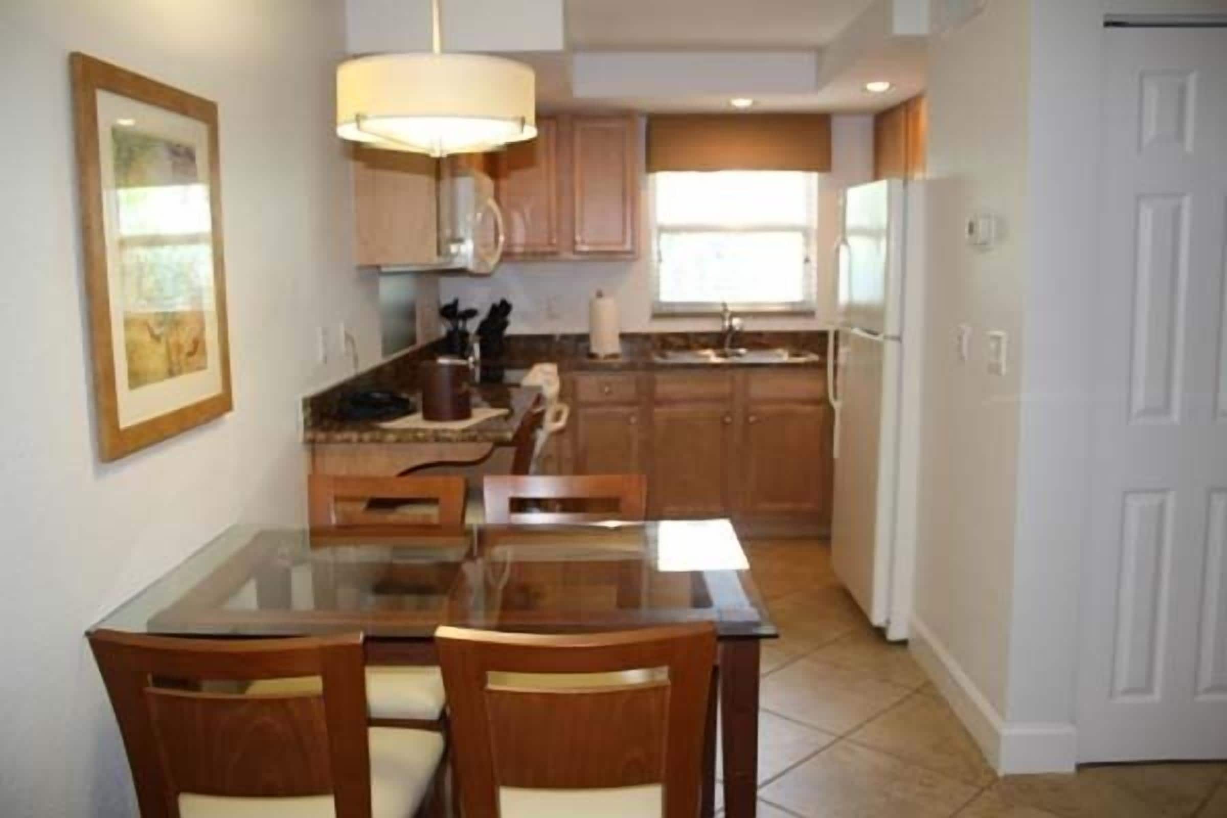 A kitchen with wooden cabinets, a glass dining table, and a white refrigerator.