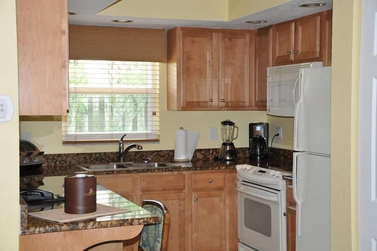 A compact kitchen with wooden cabinets, a granite countertop, a stove, and a refrigerator.