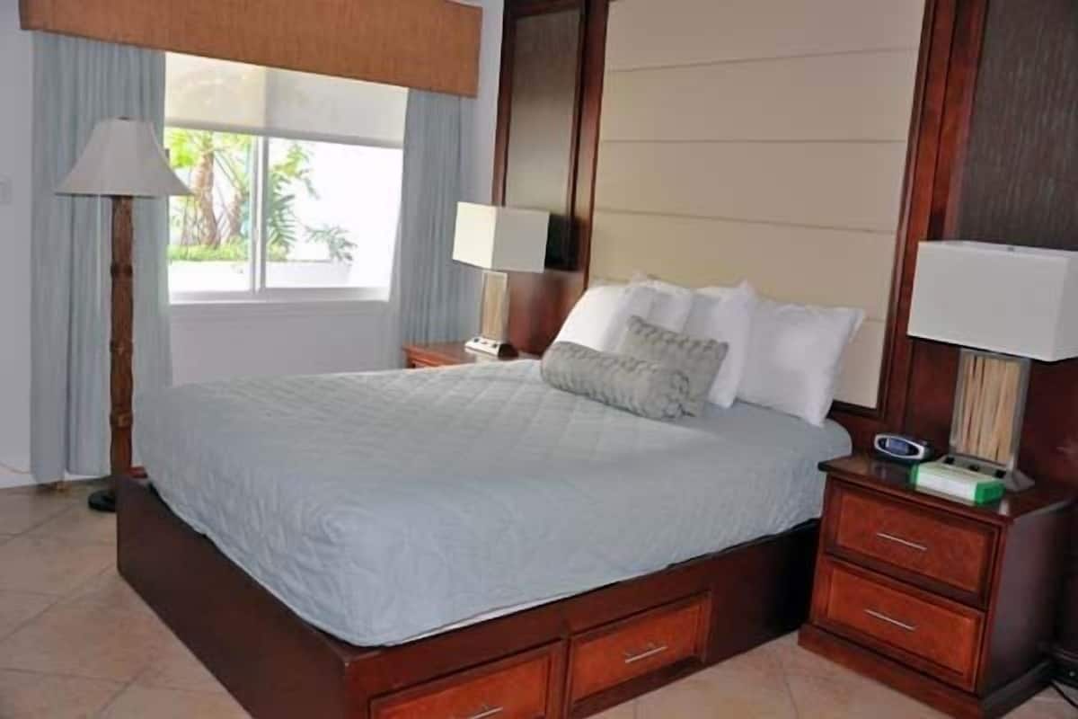 A bedroom with a large bed, wooden headboard, two bedside tables with lamps, and a window with curtains.