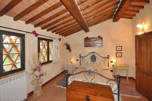 A bedroom with a wooden ceiling, a bed with a metal frame, a wooden table, and a window with a lattice design. - Podere Degli Olivi (San Gimignano)