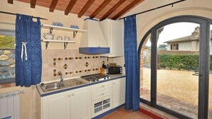 Eine Küche mit weißen Schränken, einem Gasherd und einem Toaster. Ein Fenster mit blauen Vorhängen bietet Blick auf einen Garten.