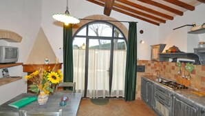 Eine Küche mit Holzbalkendecke, einem großen Fenster mit Vorhängen, einer Spüle und einem Herd.