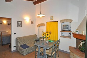 A cozy living room with a checkered sofa, a dining table with chairs, a vase of sunflowers, and a television on a shelf. - Podere Degli Olivi (San Gimignano)