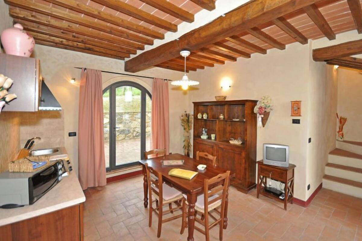 A dining area with a wooden table and chairs, a built-in oven, a television on a small stand, and a large window with curtains.
