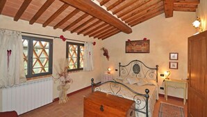 Ein Schlafzimmer mit Holzboden, einem Bett mit Metallgestell, einem Nachttisch mit Lampe und einem Fenster mit Vorhängen.