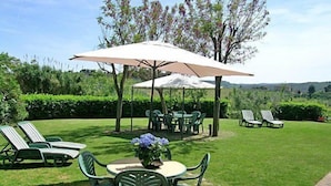 Ein Patio mit Außenmöbeln, darunter Stühle und Tische, unter einem großen Sonnenschirm.