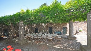 An outdoor seating area with tables and chairs under a pergola, set against a stone wall. - Il Principe (Manciano)