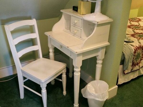 A white desk with drawers and a chair in a room with green walls and a carpeted floor.