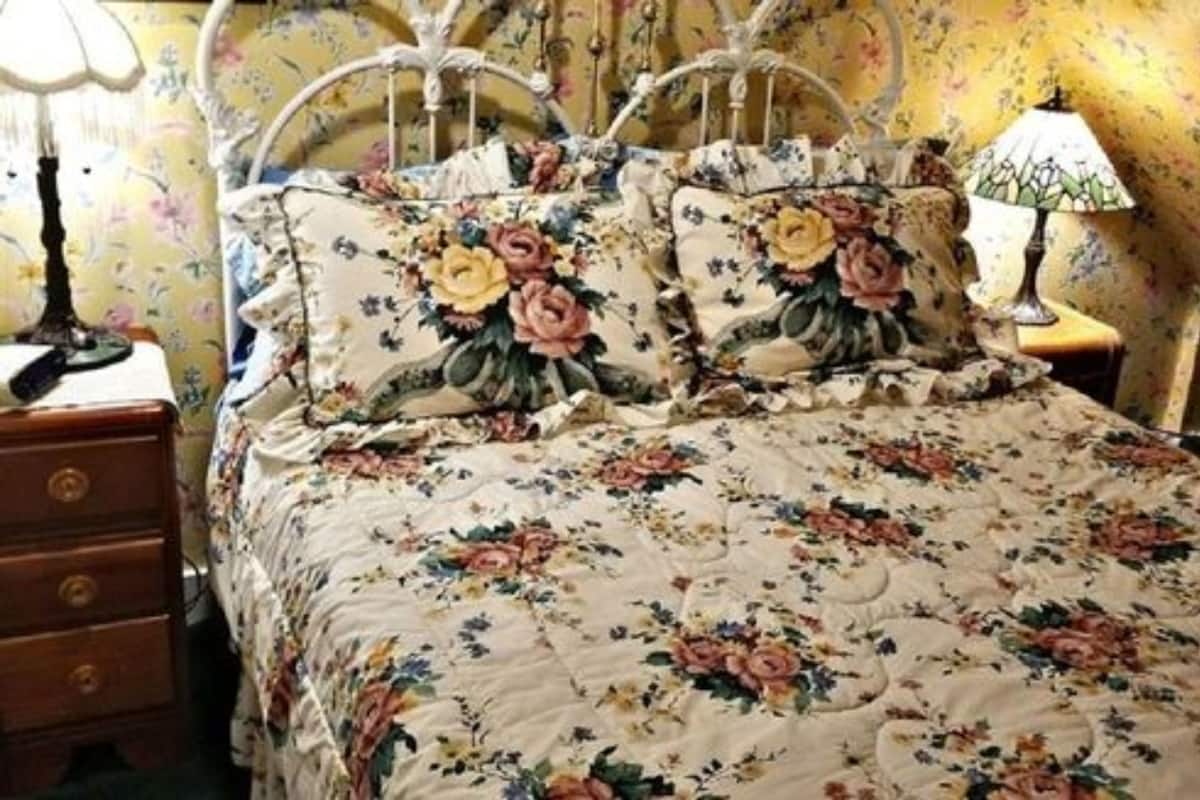 A bedroom with a floral bedspread, matching pillows, and a wooden nightstand with a lamp.
