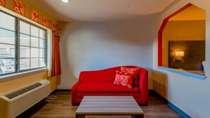 A room with a red sofa, a wooden coffee table, a window with curtains, and a wall-mounted lamp. - OYO Hotel Yoakum West (Yoakum)